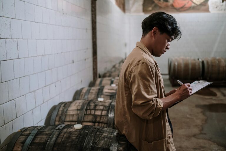 Home A craft beer expert inspects wooden barrels in a brewery's storage room.