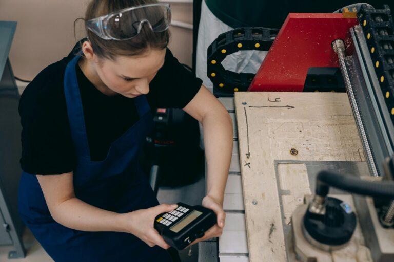 Home Woman in workshop using control device on machinery, wearing protective goggles and apron.